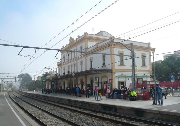 Estación de tren de Sitges vista desde las vías, con viajeros esperando en el andén