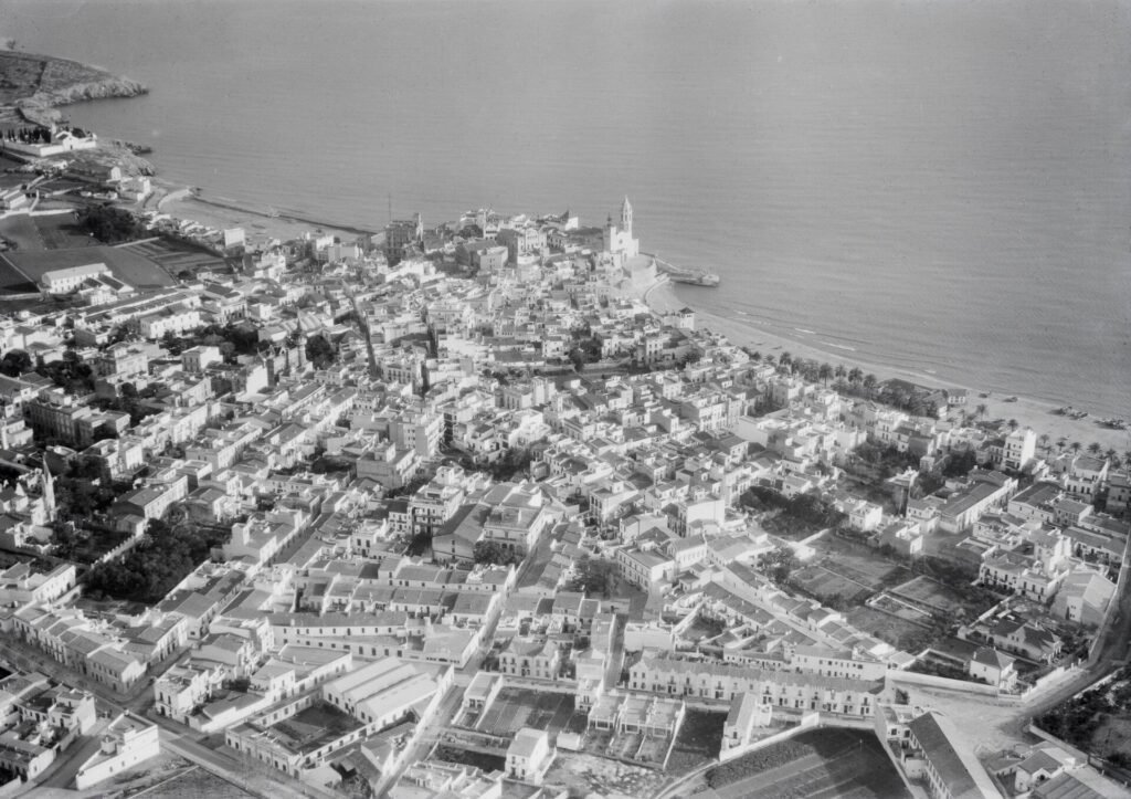 Vista aérea histórica de Sitges hacia 1930, con el promontorio de la Punta, la iglesia y el casco antiguo junto al mar