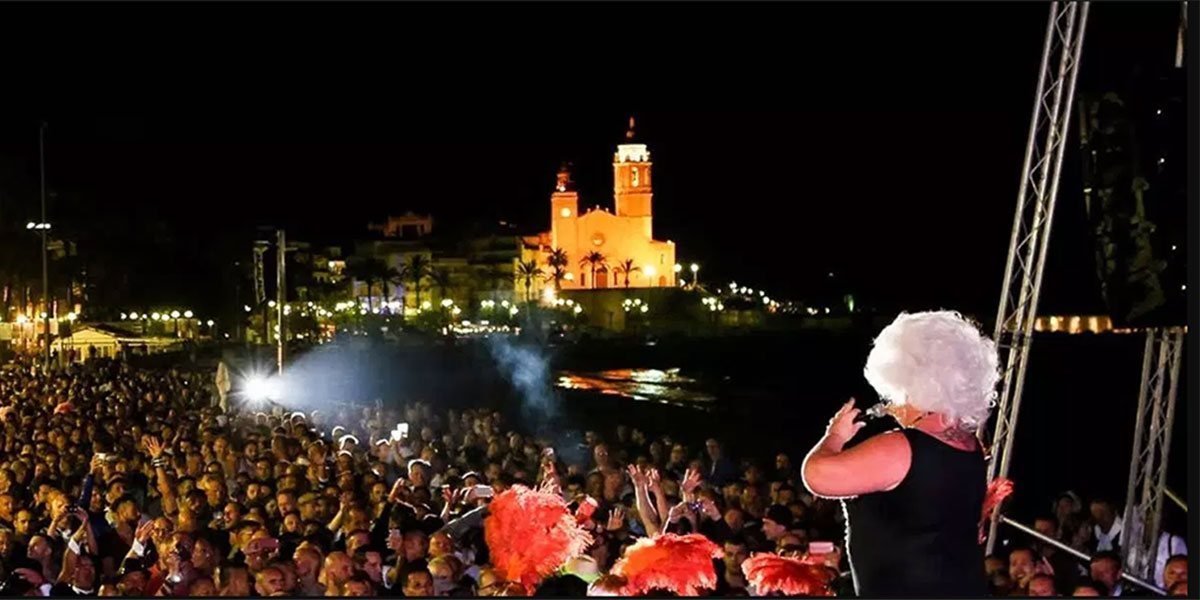 Concert del Sitges Pride de nit a la platja, amb el públic i l’església de Sant Bartomeu i Santa Tecla il·luminada al fons